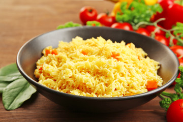 Stewed rice with a carrot on a black plate over wooden background, close up