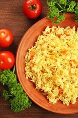 Stewed rice with a carrot on a brown plate over wooden background, close up