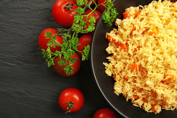 Stewed rice with a carrot and tomatoes on a plate over black background, close up