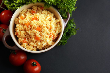 Stewed rice with a carrot and tomatoes in a cooking pot over black background, close up