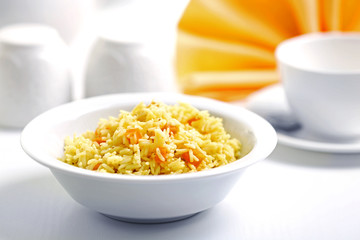 Stewed rice with a carrot in a white bowl on a table
