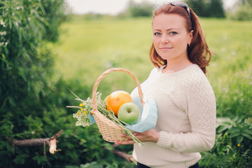 woman with a basket with apples and oranges in the summer field