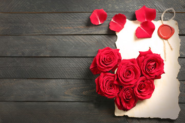 Fresh red roses buds in shape of heart with blank present card on wooden background