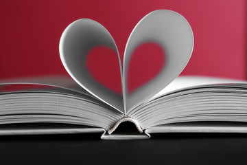 Sheets of book curved into heart shape on pink background