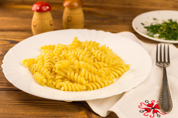 Italian pasta fusilli in plate, napkin and fork on wooden table