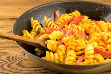 Italian pasta fusilli with tomato sauce and sausage in pan, wooden spoon on table