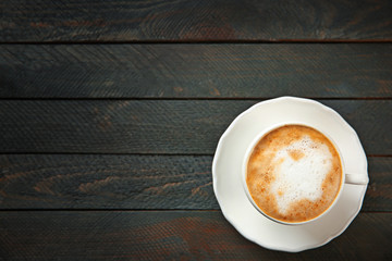 Cup of hot cappuccino with froth on a black wooden table