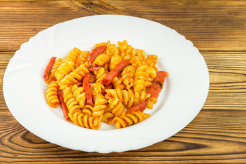 Italian pasta fusilli with tomato sauce and sausage in plate on wooden table