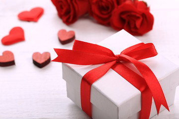 Gift box, rose flowers and decorative hearts on light wooden background