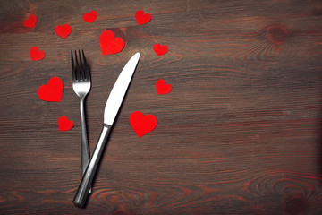 Fork and knife with decorative paper hearts, on wooden background