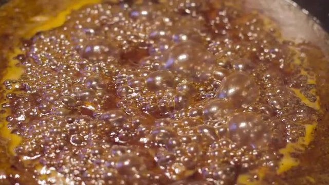 Close up of sauce caramelizing and bubbling in cast iron skillet in slow motion