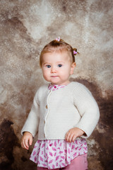 Fototapeta premium Serious little girl with blond hair and plump cheeks looking at camera. Studio portrait on brown grunge background