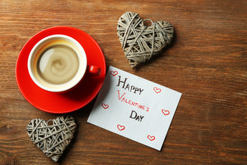 Valentine concept. Cup of coffee with grey hearts and note on wooden table background