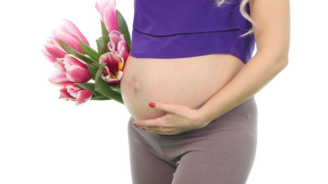 Pregnant woman holding her belly and bouquet of tulips, white, closeup