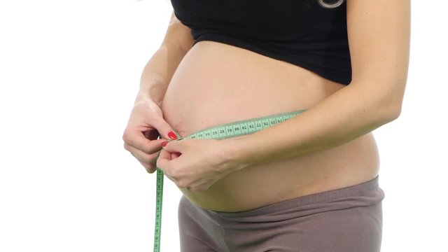 Pregnant woman measures her tummy by tape measure, white, closeup