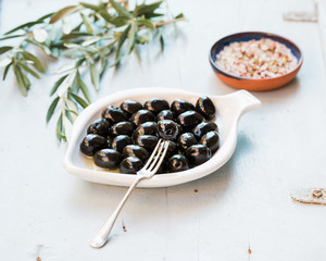 Black olives in white ceramic plate, branches and spices over li