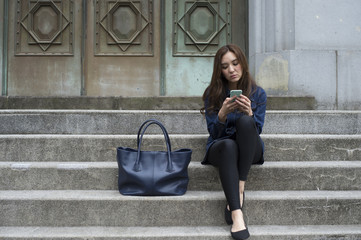 Young women are looking at the smartphone sitting on the outside of the stairs