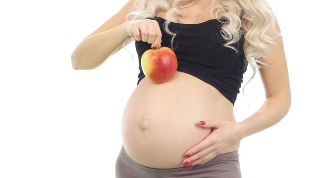 Pregnant woman with a red apple on her belly, white, closeup