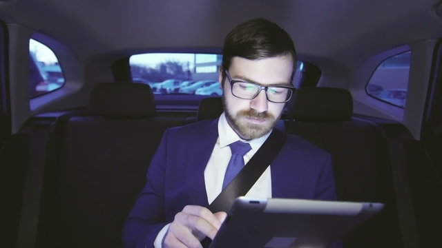 Businessman using his digital tablet in the backseat of his car during business traveling