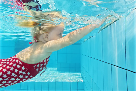 Child swimming lesson - girl learning to dive underwater in pool. Healthy active family lifestyle, physical exercise and water sports activity with parents on summer holiday with kid in aquatic center