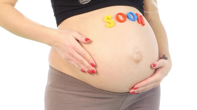  Cropped image of pregnant woman with coming soon sign on her belly standing, white, closeup