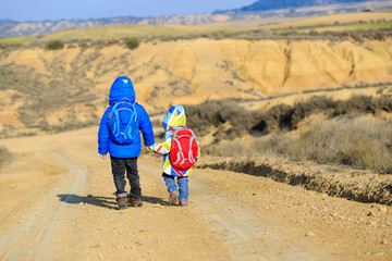 Fototapeta premium little boy and girl with backpacks travel on the road to mountains