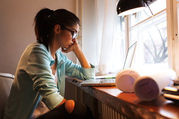 Young female student working at home.She sitting in her working room and doing something on...