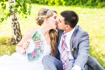Beautiful bride and groom sitting in grass and kissing. Young wedding couple
