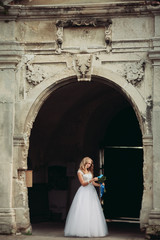 Beautiful young blond bride with bridal bouquet sitting on the stairs under gorgeous plants