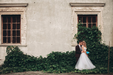 Obraz premium Luxury wedding couple hugging and smiling each other on the background gorgeous plants in castle