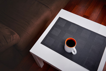 
Cup of coffee on a white coffee table in a living room. Concept of lazy afternoon.

