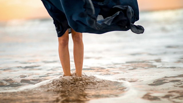 Female legs in the blue skirt flying standing on the sandy beach