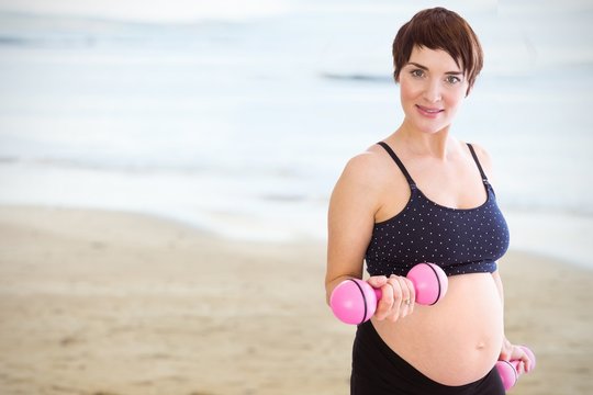 Composite image of portrait of pregnant woman lifting dumbbells