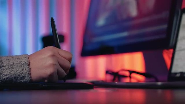 Sliding dolly shot of female designer using graphic tablet at her home office desk