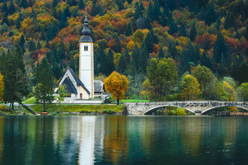 Gorgeous view of colorful autumnal scene of famous Church of St John the Baptist, Bohinj Lake, Ribicev Laz, touristic village in Slovenia