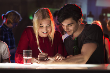 Young man is flirting with attractive woman at bar writing number on his hand