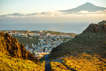 Fototapeta premium Krajobrazowy widok na górską drogę i miasto San Sebastian z wyspą Teneryfa w tle w godzinach porannych