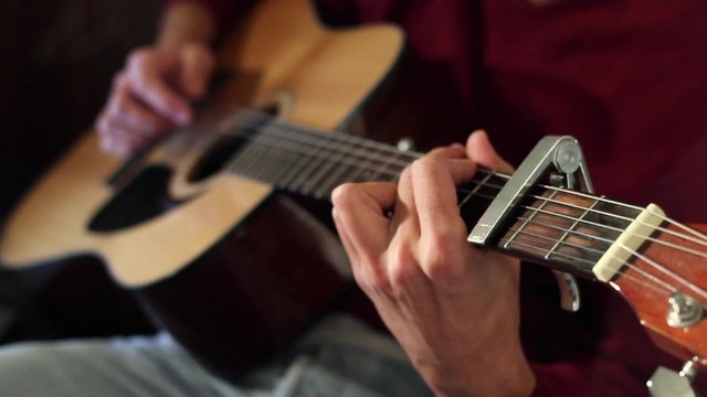 Musician Playing on Acoustic Guitar. The guitar capo attached.