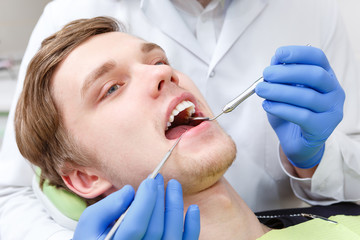 Closeup portrait of Young Man in dentist chair having teeth examined at dentists in dental office