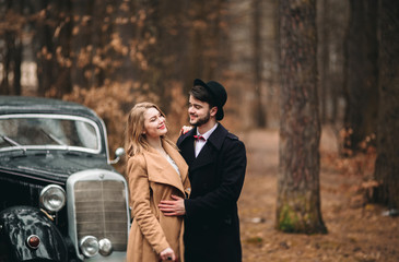 Stylish Loving wedding couple kissing and hugging in a pine forest near retro car