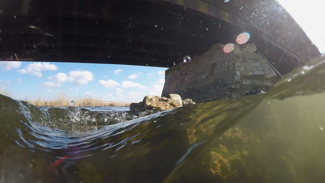 Underwater split:  Support of the old bridge made of bricks. River flowing under the bridge.