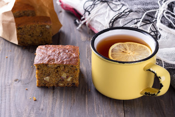 Homemade carrot and banana cake with nuts and spices, a cup of tea with lemon on a wooden surface 