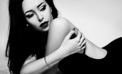 beautiful elegant brunette woman in a black dress with a bare back with makeup, hair, manicure. Art black and white photo in the studio