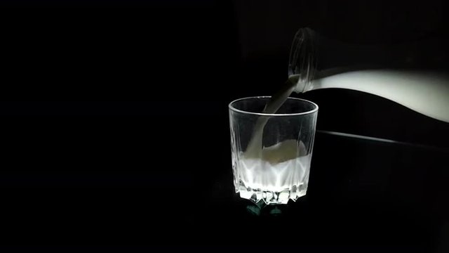 pour milk in glass on black background