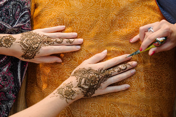 applying henna tattoo on women hands