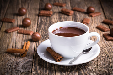 White cup of delicious hot chocolate with candies on table.
