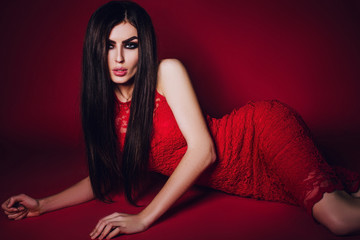 Naklejka premium Long hair. beautiful elegant brunette girl model in a red lace dress, with makeup smoky eyes, red catkins on a red background in studio 