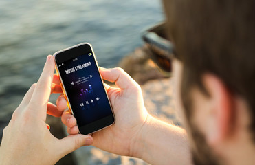 Man using his mobile phone on the coast to listen music streamin