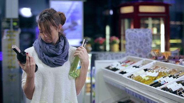 Attractive girl cant make choise in buying wine