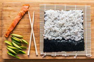 Preparing sushi. Salmon, avocado, rice and chopsticks on wooden table.